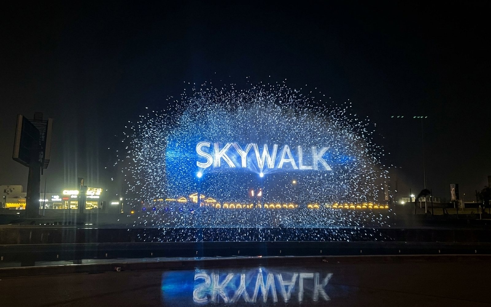 SKYWALK's water screen projecting a lit geometric pattern above the fountain at night